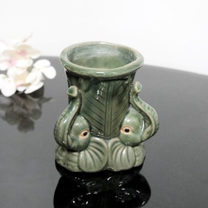 May include: A green ceramic vase shaped like two elephants with their trunks intertwined. The vase has a leafy design and is perfect for displaying flowers.