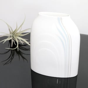 May include: White ceramic vase with a light blue and gold design. The vase has a rounded rectangular shape and a wide opening.