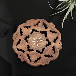 May include: A round wooden coaster with intricate carvings and a white floral design in the centre.
