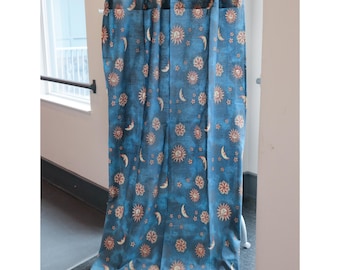 May include: A pair of blue curtains with a repeating pattern of suns and moons. The curtains are hung on a white rod.