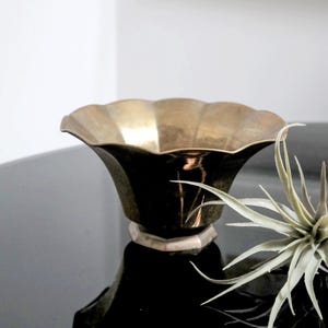 May include: A brass planter with a scalloped rim and a hexagonal base. The planter is sitting on a black surface.