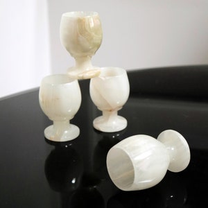 May include: Four white onyx shot glasses with a swirl pattern, stacked in a pyramid shape on a black surface.