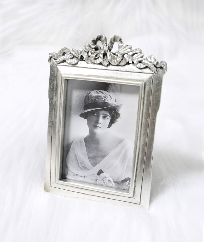 Pu&ograve; includere: Cornice per foto argentata con un designo ornato e una foto in bianco e nero di una donna con un cappello. La foto &egrave; etichettata "Dimensione: 3,5" x 5" "