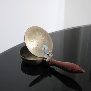 May include: A brass and wood ashtray with an engraved design on the lid. The lid is open and the ashtray is sitting on a black surface.