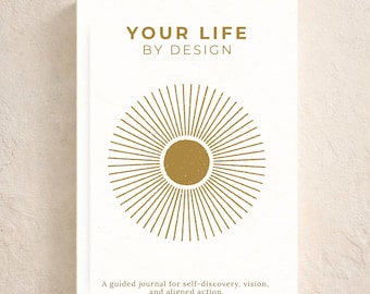 May include: A white rectangular journal with the text "YOUR LIFE BY DESIGN" in gold, featuring a gold sunburst graphic. Below the graphic, the text reads "A guided journal for self-discovery, vision, and aligned action." The bottom text reads "A journey within."