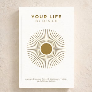 May include: A white journal with gold text reading "YOUR LIFE BY DESIGN" and a gold sunburst design. The text "Guided Journal for Clarity & Direction" is at the top. The bottom text reads "A guided journal for self-discovery, vision, and aligned action."