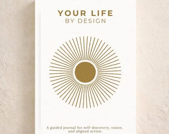 May include: A white journal with gold text and a sunburst design. The cover reads "YOUR LIFE BY DESIGN" and "Guided Journal for Clarity & Direction." The journal's description says it is for self-discovery, vision, and aligned action.
