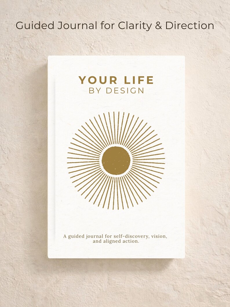 May include: A white journal with gold text and a sunburst design. The cover reads "YOUR LIFE BY DESIGN" and "Guided Journal for Clarity & Direction." The journal's description says it is for self-discovery, vision, and aligned action.