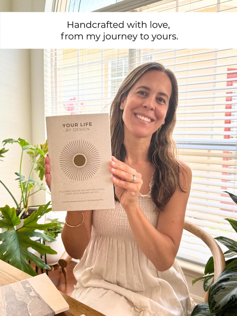 May include: A woman holding a journal titled "YOUR LIFE BY DESIGN." The journal has a beige cover with a sunburst design. The text "Handcrafted with love, from my journey to yours" is above the journal. The journal is for self-discovery, vision, and aligned action.