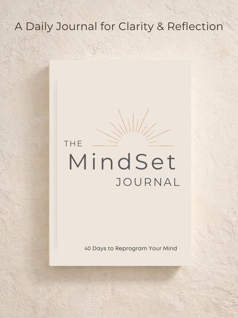 May include: A cream-coloured journal titled "The MindSet Journal" with gold accents and text that reads "A Daily Journal for Clarity & Reflection" and "40 Days to Reprogram Your Mind". The cover features a sunburst design.