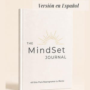Könnte beinhalten: Ein weißes Hardcover-Journal mit dem Titel The MindSet JOURNAL und einer goldenen Sonnenstrahlengrafik über dem Text. Der Einband enthält den Untertitel 40 Días Para Reprogramar tu Mente und ein Etikett Versión en Español in Schwarz.
