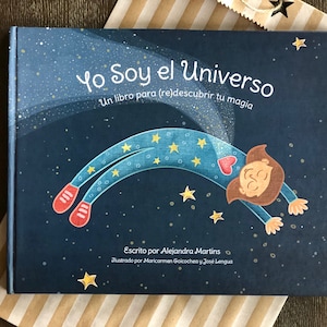 May include: A blue book with a girl floating in space with stars and the title "Yo Soy el Universo" and the text "Un libro para (re)descubrir tu magia". The book also has the text "Escrito por Alejandra Martins" and "Ilustrado por Maricarmen Goicochea y José Lengua".
