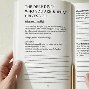 May include: An open book with the title "THE DEEP DIVE: WHO YOU ARE & WHAT DRIVES YOU." The text includes questions about self-awareness and core values. A gold pen rests on the right page. The book is held open by hands.