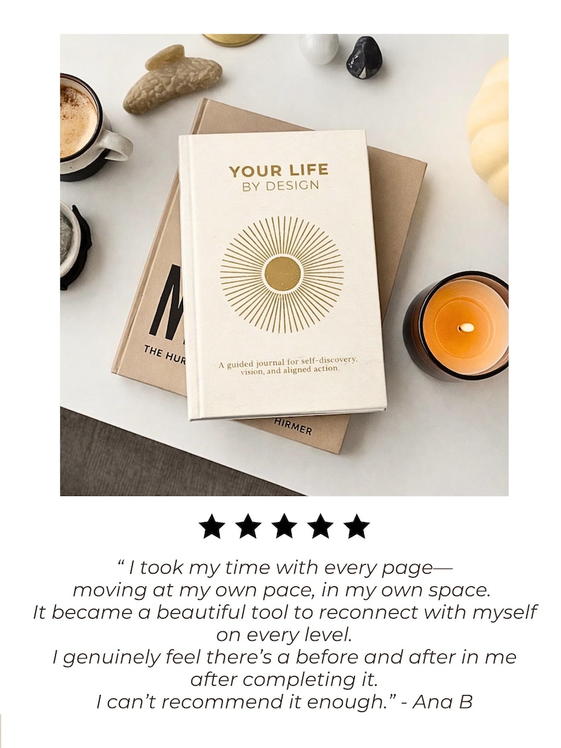 May include: A cream-colored journal titled "YOUR LIFE BY DESIGN" with a gold sunburst design. The journal is on top of a brown book, with a cup of coffee, a candle, and decorative stones nearby. The journal is described as a guided journal for self-discovery.
