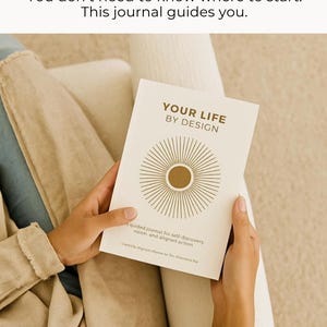 May include: A cream-colored journal titled "YOUR LIFE BY DESIGN" with a gold sunburst design. The journal is held open, revealing text about self-discovery and aligned action. The image also includes the text "You don't need to know where to start. This journal guides you."