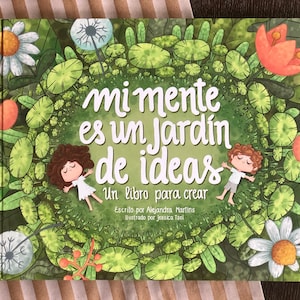 May include: A green book cover with a colorful illustration of a garden with two children lying down. The title of the book is "Mi mente es un jardin de ideas" and the subtitle is "Un libro para crear". The book is written by Alejandra Martins and illustrated by Jessica Tsol.