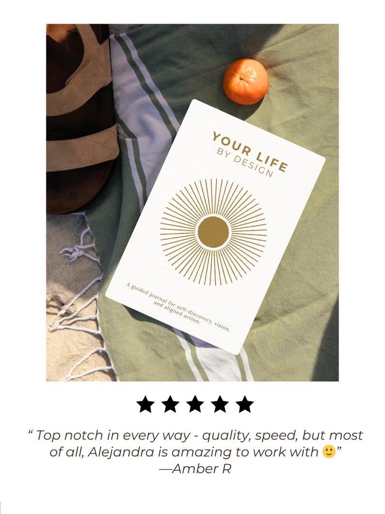 May include: A white journal titled "YOUR LIFE BY DESIGN" with gold sunburst design, resting on a green and white striped towel. A small orange fruit and a pair of brown sandals are also visible. The journal's text reads: "A guided journal for self-discovery, vision, and aligned action."