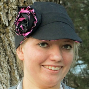 May include: A black and pink baseball cap with a large pink flower on the side. The cap has a curved brim and a soft, fabric texture.