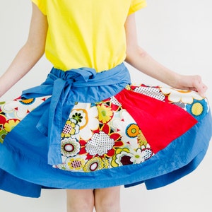 Peut inclure: Une jupe en patchwork bleu, rouge et blanc avec un imprimé floral. La jupe est nouée à la taille avec une ceinture bleue.