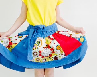May include: A blue, red and white patchwork skirt with a floral print. The skirt is tied at the waist with a blue sash.