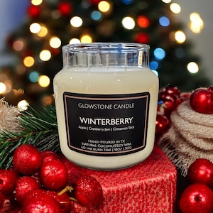May include: A large glass jar candle with a black label that reads "WINTERBERRY" with apple, cranberry jam, and cinnamon stick scents. The candle is hand-poured in Texas with natural coconut soy wax and has a 60+ hour burn time. The candle is 18oz / 510g.