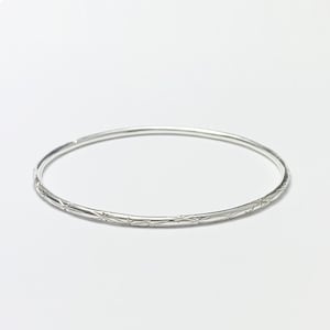 May include: A silver bangle bracelet with a delicate star pattern engraved around the entire circumference.