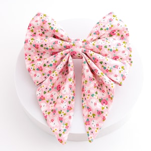May include: A large pink fabric bow with a floral and bunny pattern. The bow is made of a soft material and is tied in the center. The bow is on a white surface.