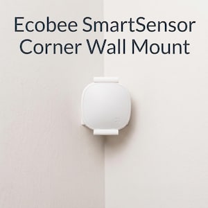 May include: A white Ecobee SmartSensor Corner Wall Mount is mounted in the corner of two white walls. The mount is square with rounded edges and has two small, rectangular brackets. The text "Ecobee SmartSensor Corner Wall Mount" is at the top.