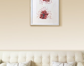 May include: A framed artwork featuring two abstract floral designs in red, green, and yellow. The artwork is displayed in a white frame and hangs above a cream-colored sofa with marble-patterned pillows.