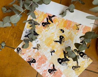 May include: Two art prints featuring a repeating pattern of black bird illustrations on a floral background in shades of yellow, orange, and white. Eucalyptus branches with green leaves are arranged around the prints.