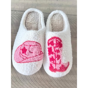 May include: A pair of white fuzzy slippers with pink embroidered cowboy hats and boots.