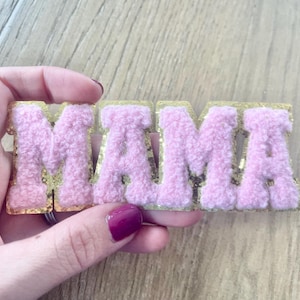 May include: Pink fluffy letters spelling out "MAMA" with gold glitter trim.