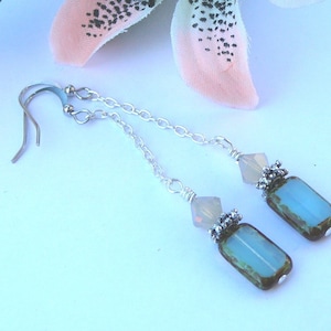 May include: A pair of silver dangle earrings with a light blue and green rectangular glass bead and a small white bead on each earring.