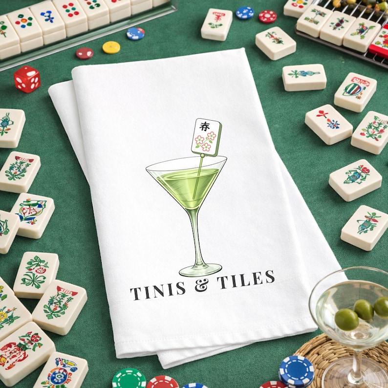 May include: White kitchen towel with a martini glass illustration and the text "TINIS & TILES". The martini glass contains a green liquid and a decorative garnish. Mahjong tiles are scattered around the towel.