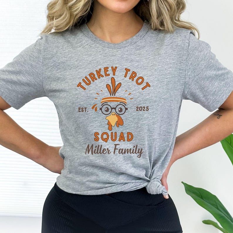 May include: A heather gray t-shirt with a turkey graphic and the text "TURKEY TROT SQUAD Miller Family EST. 2025". The graphic features a turkey wearing glasses and a headband. The shirt is a crew neck.