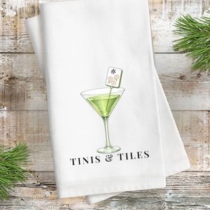 May include: White kitchen towel with a martini glass illustration and the text "TINIS & TILES". The martini glass contains a green liquid and a decorative garnish. Mahjong tiles are scattered around the towel.