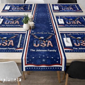Puede incluir: Una mesa decorada con manteles individuales y un camino de mesa de temática patriótica. El diseño incluye la palabra "USA" en rojo, blanco y azul, un águila y los textos "Faith, Family and Freedom" y "The Johnson Family".