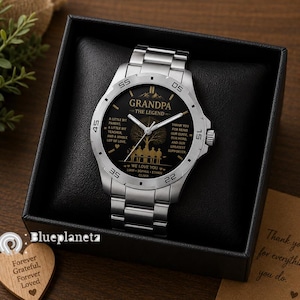 May include: A silver-tone stainless steel wristwatch with a black dial featuring gold-colored text that reads GRANDPA THE LEGEND, along with a tree graphic, a silhouette of people on a bench, and the names LIAM, SOPHIA, ETHAN, and OLIVIA.