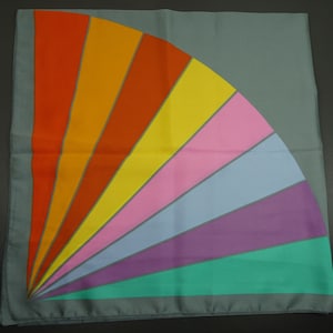 Könnte beinhalten: Ein grauer Seidenschal mit einem bunten Regenbogenmuster. Der Schal hat ein fächerförmiges Muster aus orangefarbenen, gelben, rosa, blauen, violetten und grünen Streifen.