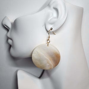 May include: A pair of gold hoop earrings with a large, round, white and brown shell pendant.