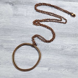 Op de afbeelding: Een koperen ketting met een grote, ronde hanger. De hanger is een eenvoudige cirkel met een licht onregelmatige vorm.