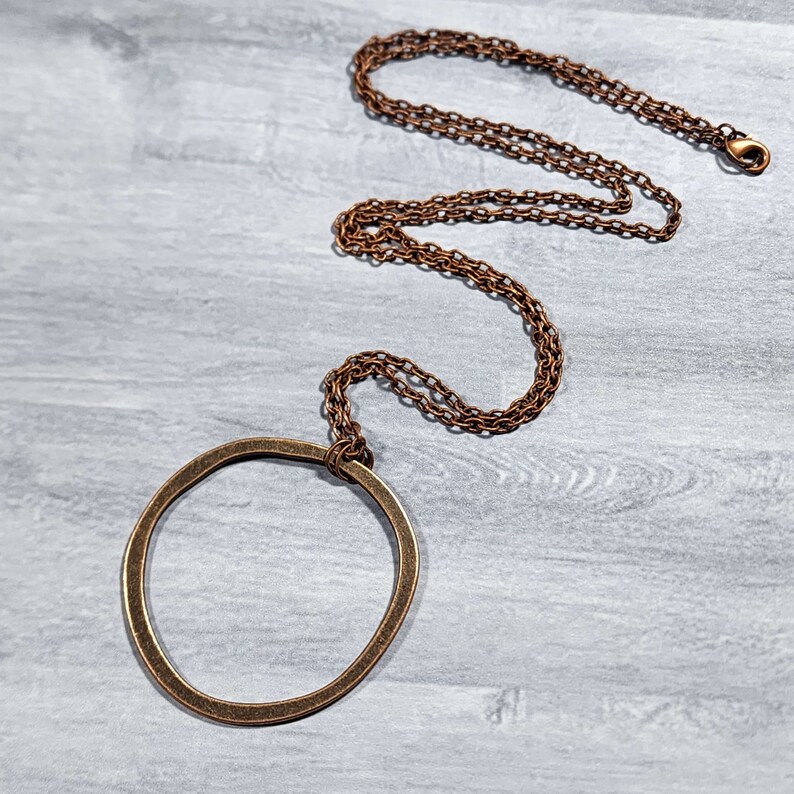 Op de afbeelding: Een koperen ketting met een grote, ronde hanger. De hanger is een eenvoudige cirkel met een licht onregelmatige vorm.