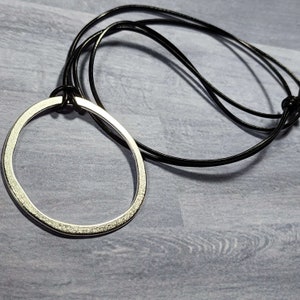 May include: A silver circle pendant necklace with a textured surface, hanging from a black leather cord.