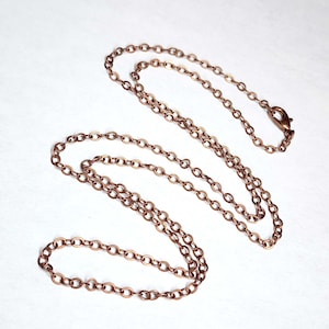 May include: A copper-colored necklace with a delicate chain design. The necklace features small, oval-shaped links and a lobster clasp closure. The chain is approximately 20 inches long.