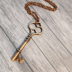 May include: A gold-toned key necklace with a heart-shaped key pendant. The key has intricate details and a vintage style.