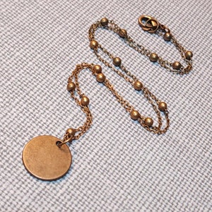 May include: A gold-toned necklace with a round pendant. The necklace has a double chain with small beads.