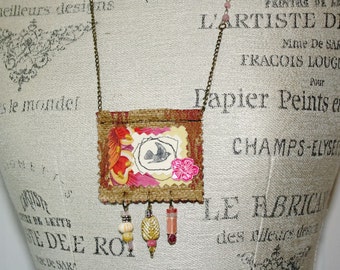May include: A brown burlap necklace with a rectangular pendant featuring a collage of fabric, paper, and embellishments. The pendant has a pink flower, a bird silhouette, and a red and orange floral design. The necklace has a chain with a pink bead and a variety of colourful beads hanging from the pendant.