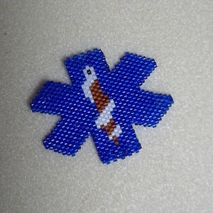 以下が含まれることがあります： 青と白のビーズでできたライフスターのチャーム。ライフスターは救急医療サービスで使用されるシンボルです。