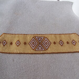 May include: A beaded bracelet with a geometric pattern in shades of brown and white.