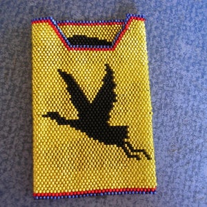 May include: A gold beaded phone case with a black silhouette of a bird in flight.